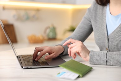 Photo of Woman using laptop at white marble table with passport and flight ticket indoors, closeup