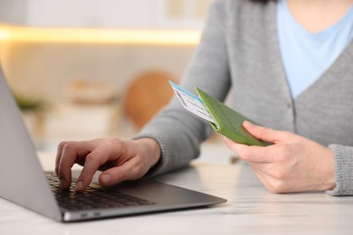 Photo of Woman with passport and flight ticket using laptop at white marble table indoors, closeup