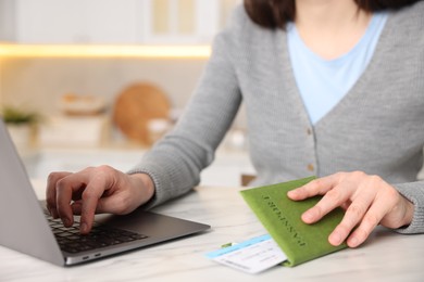 Photo of Woman with passport and flight ticket using laptop at white marble table indoors, closeup