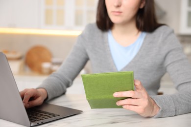 Photo of Woman with passport using laptop at marble table indoors, closeup