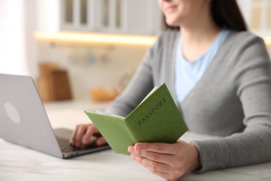 Photo of Woman with passport using laptop at marble table indoors, closeup