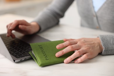 Photo of Woman with passport using laptop at white marble table indoors, closeup