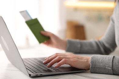 Photo of Woman with passport and flight ticket using laptop at white marble table indoors, closeup