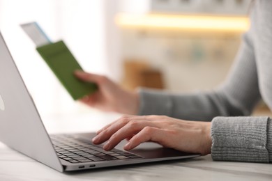 Photo of Woman with passport and flight ticket using laptop at white marble table indoors, closeup
