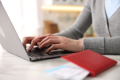 Photo of Woman using laptop at white marble table with passport and flight tickets indoors, closeup