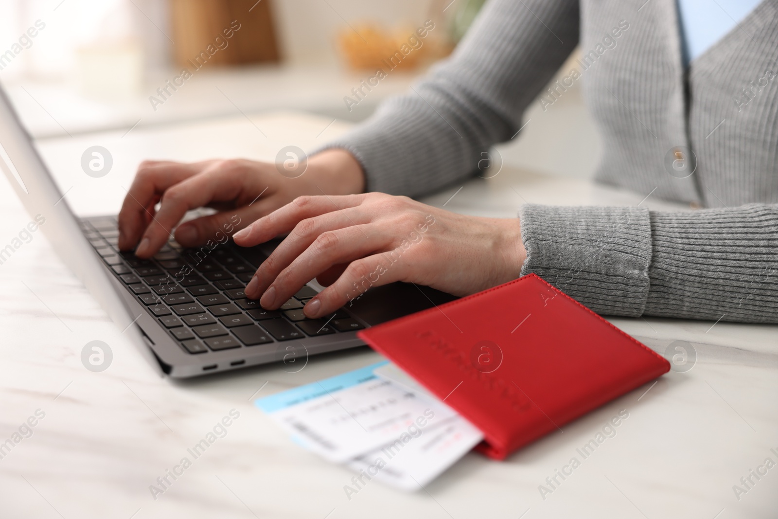 Woman using laptop at white marble table with passport and flight tickets indoors, closeup Photo of Woman using laptop at white marble table with passport and flight tickets indoors, closeup