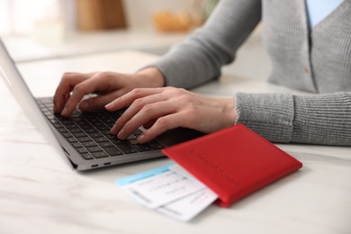 Photo of Woman using laptop at white marble table with passport and flight tickets indoors, closeup