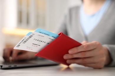 Photo of Woman with passport and flight tickets using laptop at table indoors, closeup