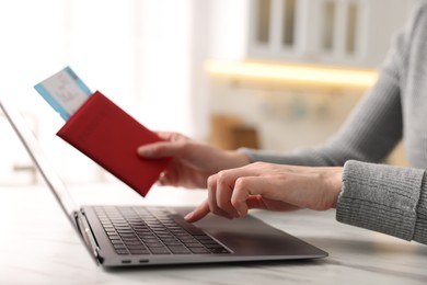 Photo of Woman with passport and flight ticket using laptop at white marble table indoors, closeup