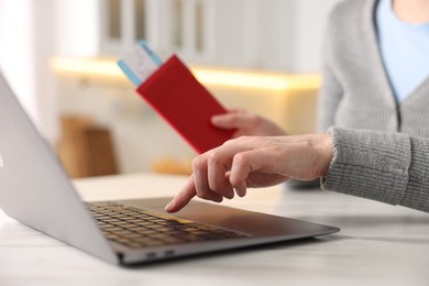 Photo of Woman with passport and flight ticket using laptop at white marble table indoors, closeup