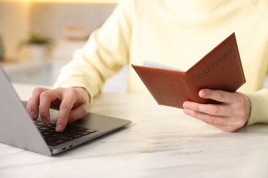 Photo of Woman with passport using laptop at white marble table indoors, closeup