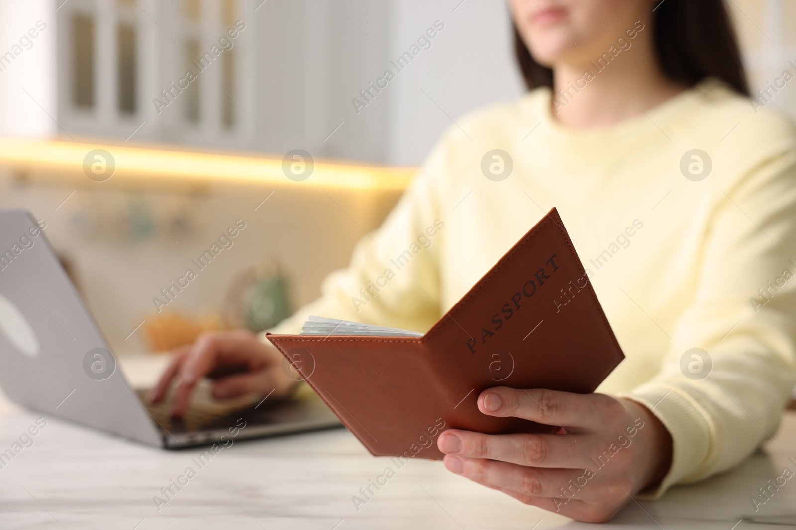 Woman with passport using laptop at white marble table indoors, closeup Photo of Woman with passport using laptop at white marble table indoors, closeup