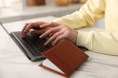 Photo of Woman using laptop at white marble table with passport indoors, closeup