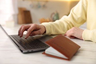 Photo of Woman using laptop at white marble table with passport indoors, closeup