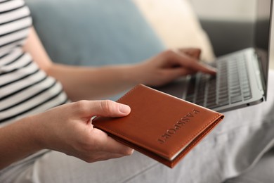 Photo of Woman with passport using laptop on sofa indoors, closeup