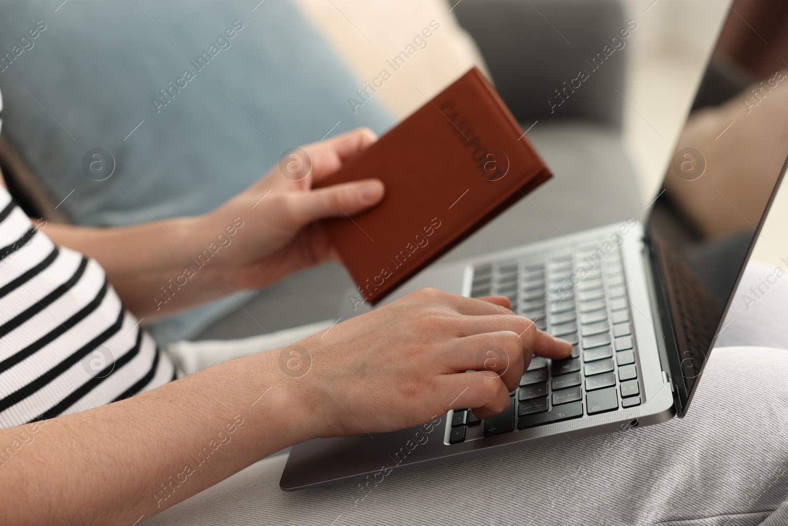 Woman with passport using laptop on sofa indoors, closeup Photo of Woman with passport using laptop on sofa indoors, closeup
