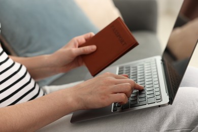 Photo of Woman with passport using laptop on sofa indoors, closeup