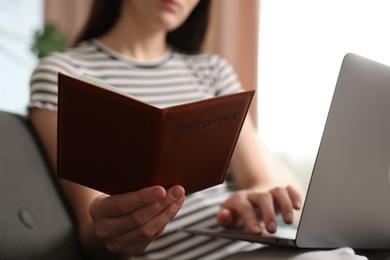 Photo of Woman with passport using laptop on sofa indoors, closeup