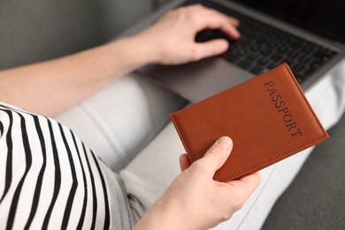 Photo of Woman with passport using laptop on sofa indoors, above view