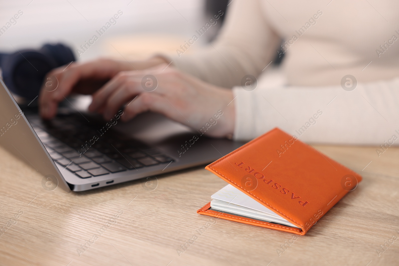 Woman using laptop at wooden table with passport indoors, closeup Photo of Woman using laptop at wooden table with passport indoors, closeup