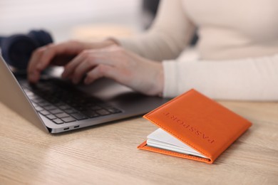 Photo of Woman using laptop at wooden table with passport indoors, closeup