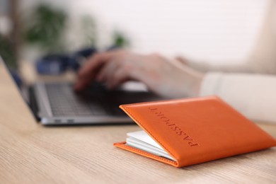 Photo of Woman using laptop at wooden table with passport indoors, closeup