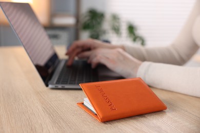 Photo of Woman using laptop at wooden table with passport indoors, closeup