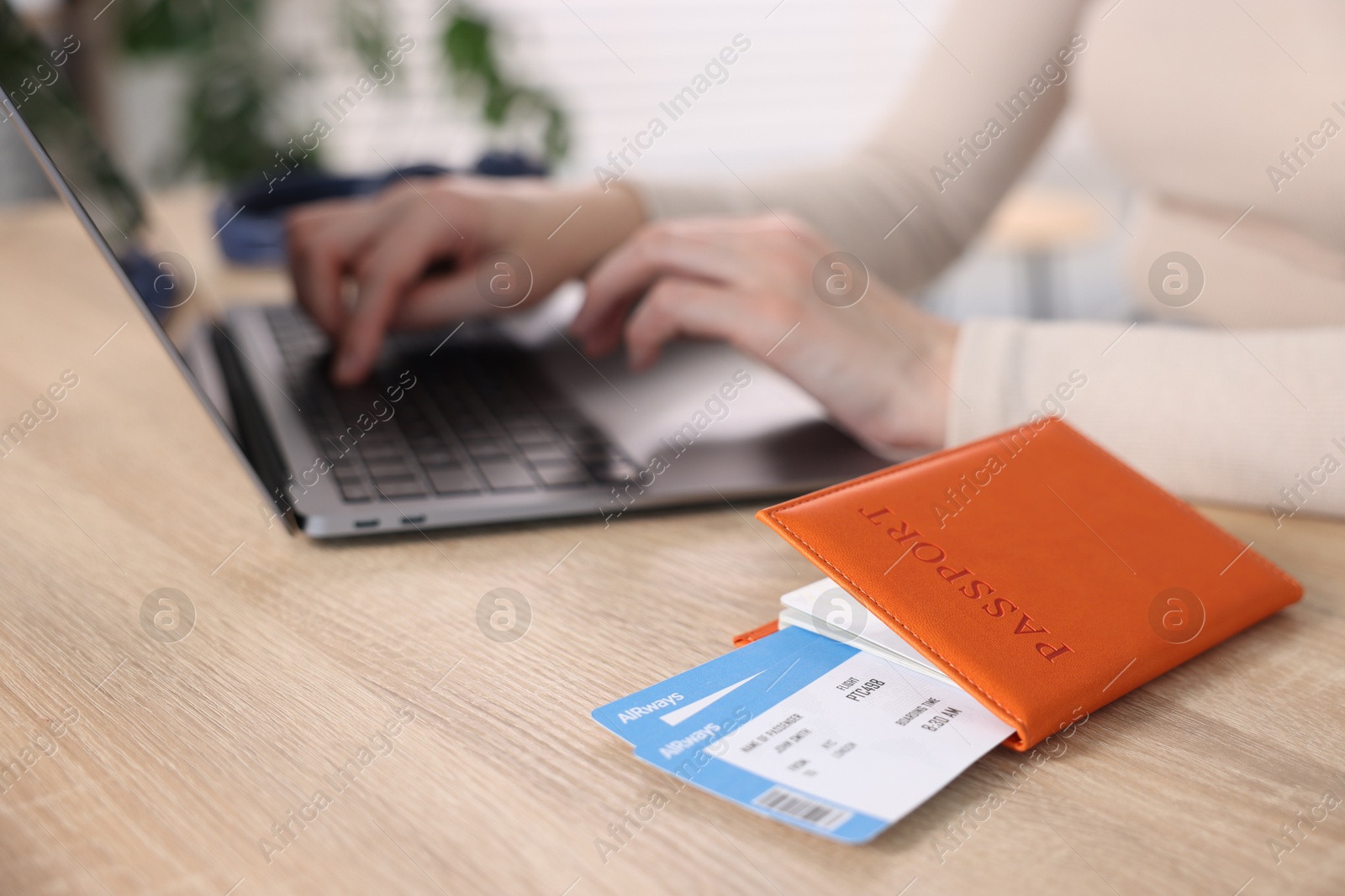Woman using laptop at wooden table with passport and flight tickets indoors, closeup Photo of Woman using laptop at wooden table with passport and flight tickets indoors, closeup