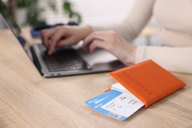 Photo of Woman using laptop at wooden table with passport and flight tickets indoors, closeup