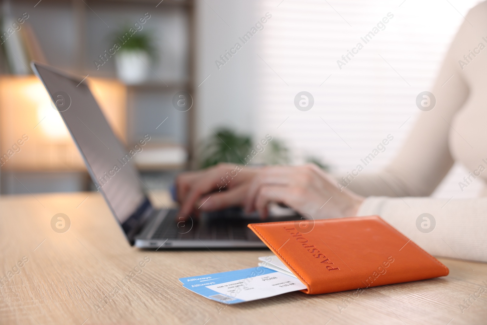 Woman using laptop at wooden table with passport and flight tickets indoors, closeup Photo of Woman using laptop at wooden table with passport and flight tickets indoors, closeup