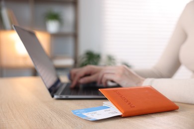 Photo of Woman using laptop at wooden table with passport and flight tickets indoors, closeup