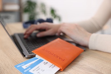 Photo of Woman using laptop at wooden table with passport and flight tickets indoors, closeup