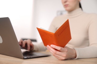 Photo of Woman with passport using laptop at table indoors, closeup