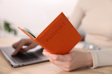 Photo of Woman with passport using laptop at table indoors, closeup