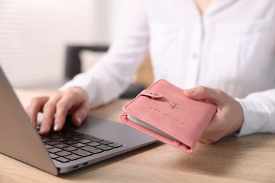 Photo of Woman with passport using laptop at wooden table indoors, closeup