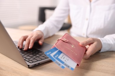 Photo of Woman with passport and flight tickets using laptop at wooden table indoors, closeup