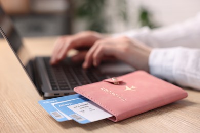 Photo of Woman using laptop at wooden table with passport and flight tickets indoors, closeup