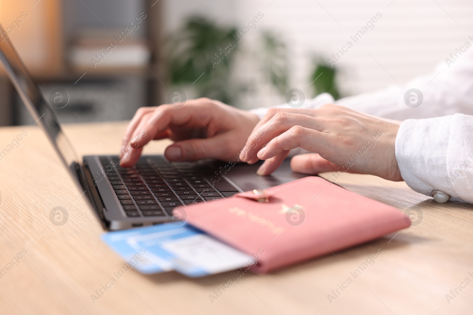 Woman using laptop at wooden table with passport and flight tickets indoors, closeup Photo of Woman using laptop at wooden table with passport and flight tickets indoors, closeup