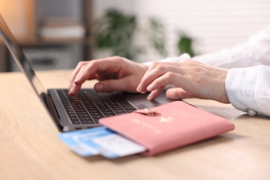 Photo of Woman using laptop at wooden table with passport and flight tickets indoors, closeup
