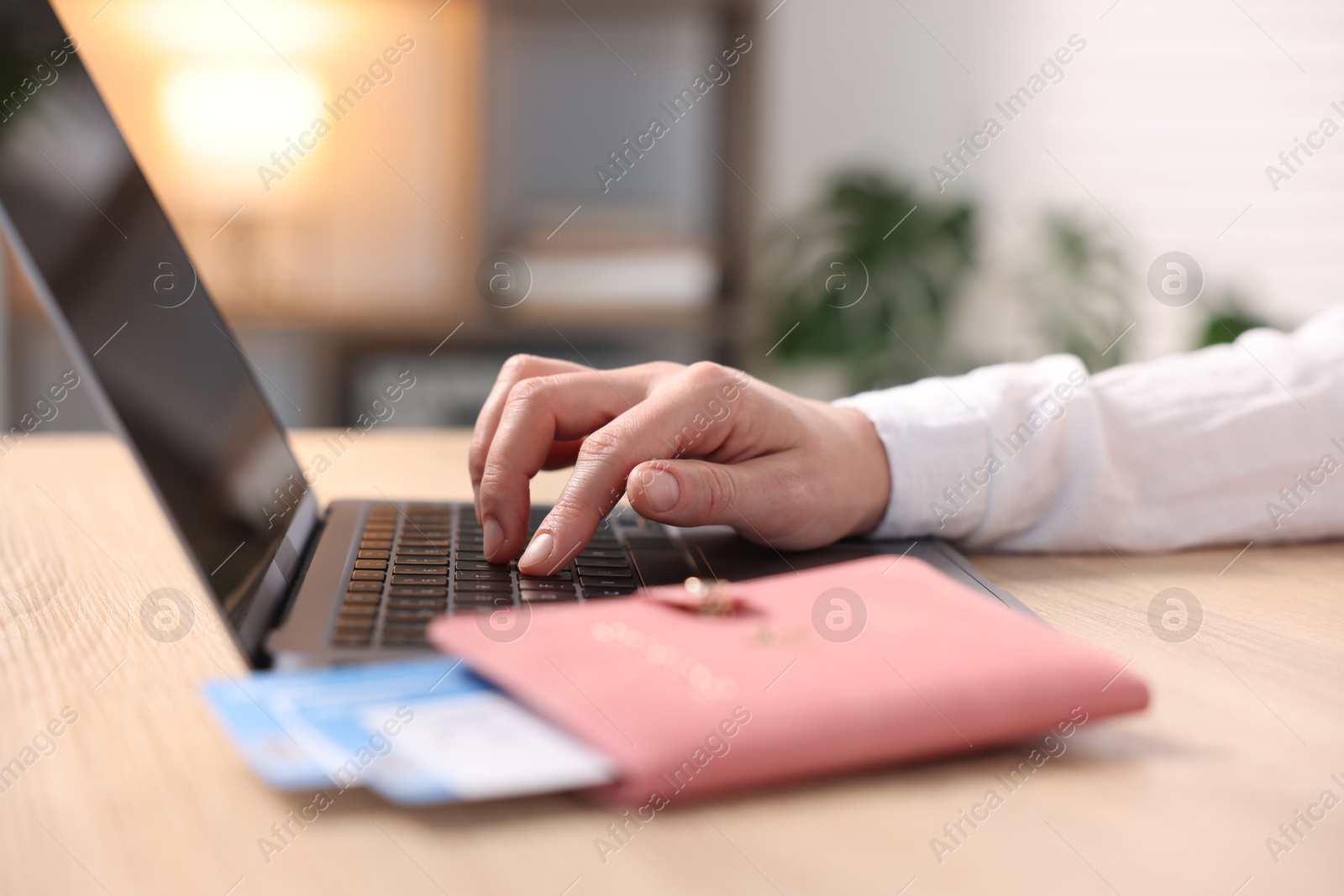 Woman using laptop at wooden table with passport and flight tickets indoors, closeup Photo of Woman using laptop at wooden table with passport and flight tickets indoors, closeup