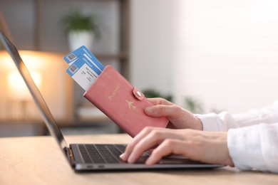Photo of Woman with passport and flight tickets using laptop at table indoors, closeup