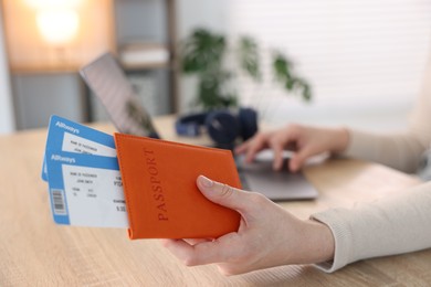 Photo of Woman with passport and flight tickets using laptop at wooden table indoors, closeup
