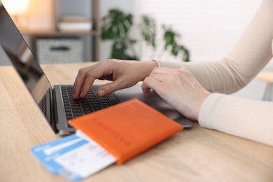 Photo of Woman using laptop at wooden table with passport and flight tickets indoors, closeup