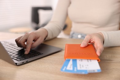 Photo of Woman with passport and flight tickets using laptop at wooden table indoors, closeup