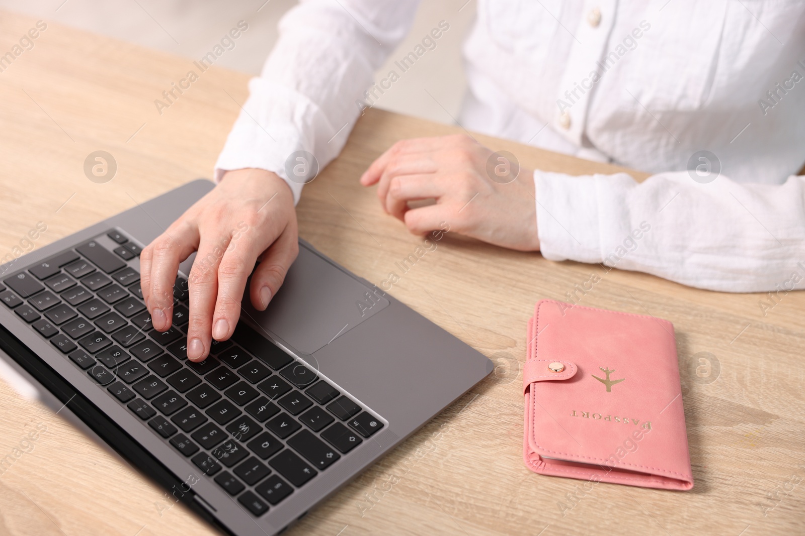 Woman using laptop at wooden table with passport indoors, closeup Photo of Woman using laptop at wooden table with passport indoors, closeup