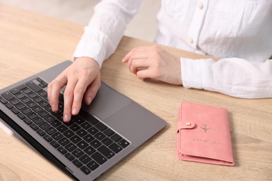 Photo of Woman using laptop at wooden table with passport indoors, closeup