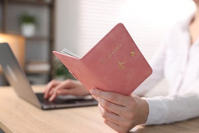 Photo of Woman with passport using laptop at table indoors, closeup