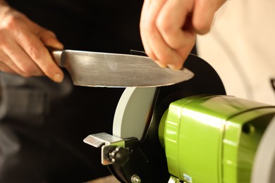 Photo of Man sharpening knife with bench grinder indoors, closeup