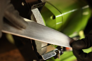 Photo of Man sharpening knife with bench grinder indoors, closeup
