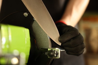 Photo of Man sharpening knife with bench grinder indoors, closeup